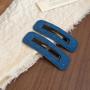 Close-up of two blue denim fabric hair clips on a textured background with fringe