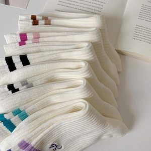 White cotton crew socks with colorful striped ribbing displayed in a cozy minimalist set
