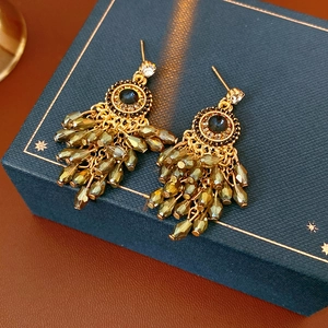Macro shot of bohemian gold earrings with olive green tassels and dark gemstone details