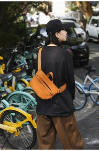 Outdoor shot of an orange nylon crossbody bag showing the adjustable strap and zipper details