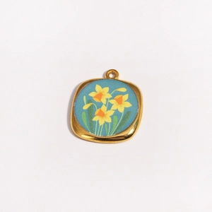 Détail d'un pendentif carré doré avec émail bleu et motif floral de jonquilles jaunes