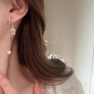 Close-up of golden tassel earrings with pearls worn by a model on light background