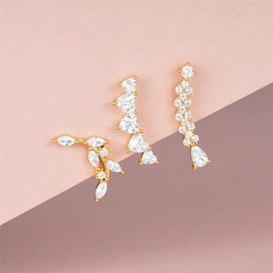 Detailed view of three gold-plated silver earrings with white zircon on pink background