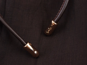 Detail shot of golden metal tips on dark brown drawstring against textured fabric