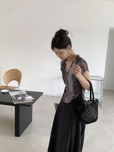 Detail of a chic black woven bucket bag styled with a purple tie-dye V-neck shirt and skirt