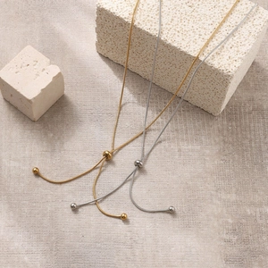 Adjustable 18k gold and silver snake chain necklaces displayed on a stone background