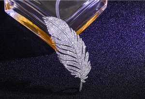 Macro detail of elegant silver feather brooch with sparkling zircons on blue background