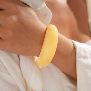 Close-up of a wide minimalist cream resin cuff bracelet worn against white linen