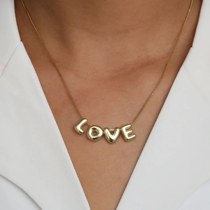 Close-up of 18k gold-plated bubble letter LOVE pendants worn on a delicate chain