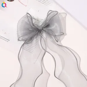 Detail of grey organza bow hair clip with long ribbons on artistic paper background