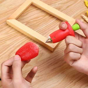 Close-up of a stainless steel strawberry huller removing a stem on a wooden table