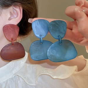 Close-up of geometric acrylic drop earrings featuring marble textures in red and blue colors