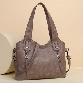 Brown faux leather handbag with silver zippers and detachable shoulder strap on a studio prop