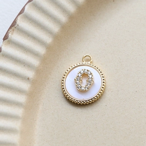 Macro view of gold plated shell pendant with letter 0 and inlaid cubic zirconia