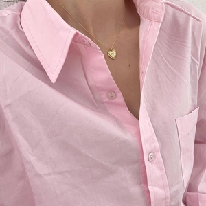 Close-up of golden heart pendant necklace with center rhinestone on pink fabric background