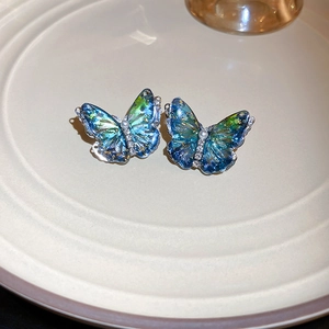 Détail macro de boucles d'oreilles papillon en résine dégradé bleu-vert et incrustation d'or