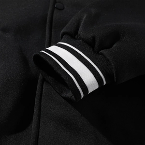 Close-up of black knit jacket showing striped ribbed cuffs and premium button details