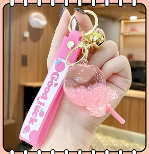 Close-up of pink lollipop keychain with flowing sand, bell, and Good Luck strap