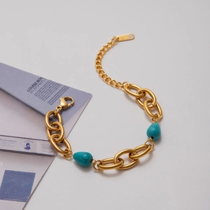 Detail of gold chain bracelet featuring turquoise charms on a light grey background