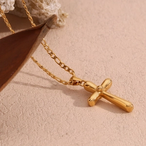 Macro shot of 18K gold plated cross pendant on a Figaro chain with natural rock background