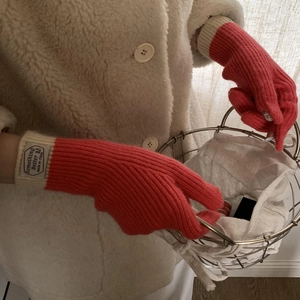 Close-up of red knit gloves with white cuffs and a woven brand label detail