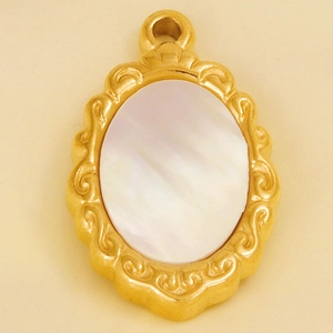 Macro shot of gold oval pendant featuring a white mother-of-pearl inlay and ornate patterns