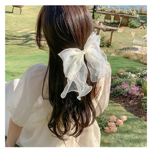 Detail of a large white organza bow hair clip with flowing ribbons on model