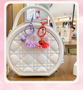 Detail of cute backpack liquid sand keychains in purple and red attached to a white handbag