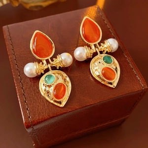 Macro shot of vintage gold earrings with red gems and pearls on a brown leather box
