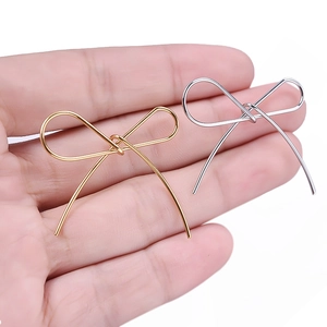Close-up of gold and silver bow-shaped stainless steel charms held in a hand