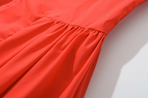 Détail d'une robe rouge montrant les coutures froncées et la texture du tissu tissé fin