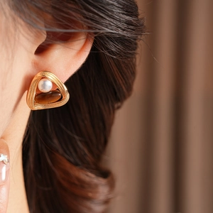 Close-up of vintage golden triangle earrings with white pearl and tiger eye stone