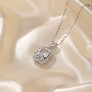 Détail macro du collier argenté avec pierre précieuse taille émeraude et halo pavé