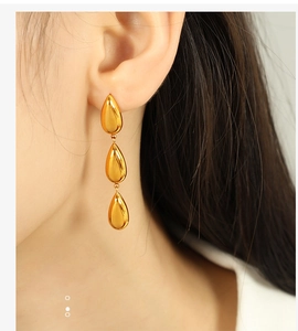 Close-up of three-tier golden waterdrop earrings worn by a model in soft lighting