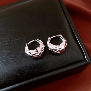 Close-up of silver U-shaped earrings with irregular pleated texture on black satin