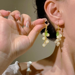 Close-up of dangling white pearl grape earrings with green leaf detail on female model