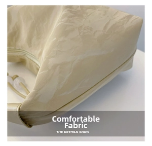 Macro shot of high-shine pleated fabric texture on a cream dumpling-style crossbody bag
