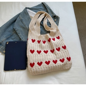 Detalle del bolso de punto crema con patrones de corazones rojos y textura calada