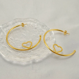 Elegant gold heart hoop earrings on a decorative glass tray with soft grey background