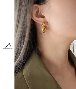 Detail of 18K gold plated stainless steel twisted C-shape hoop earring worn by model