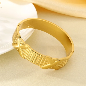 Macro detail of 18K gold plated stainless steel bangle with woven texture and X-shaped accents