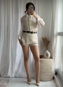 Detail of beige tweed vest and shorts set with a sleek black belt and pearl buttons