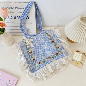 Detail of floral embroidery and white lace trim on a blue checkered canvas tote bag