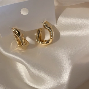 Macro shot of irregular molten gold hoop earrings on a white card with silk backdrop