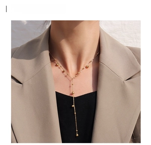 Close-up of golden Y-shaped tassel necklace with polished beads worn by model in blazer