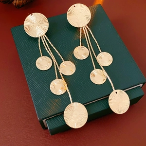Detailed close-up of golden tassel earrings with round textured studs and fine chains