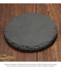 Macro shot of circular black slate coaster featuring natural raw edges on wood surface