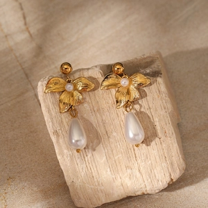 Detail of vintage gold flower earring with drop pearl on a rustic wooden display stand