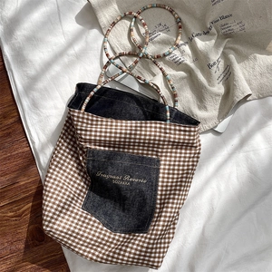 Close-up of a retro checkered canvas tote bag with a denim pocket and beaded strap