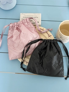Detail of pink and black drawstring bags with embossed bow texture on a wood table